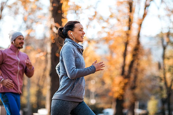 Eine jüngere Frau und ein Mann joggen draußen und sehen glücklich dabei aus. 