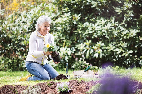 Patientin arbeitet im Garten und pflanzt Blumen ein.