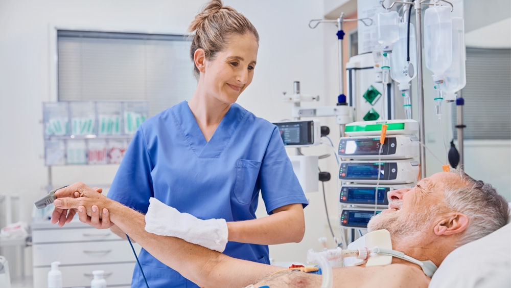 Männlicher Patient im Bett mit Krankenschwester, die an seinem Oberarm eine Körperdekolonisation durchführt