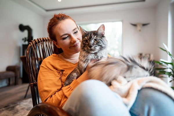 Eine junge Frau mit Stoma sitzt lächelnd auf einem Stuhl mit ihrer Katze im Schoß.