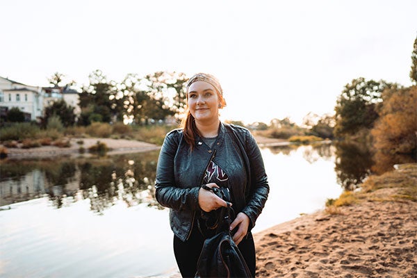 Eine junge Frau steht während der Dämmerung an einem See und lächelt.